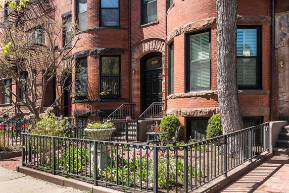 Front view of a brick multi-story building with a garden and black railing.