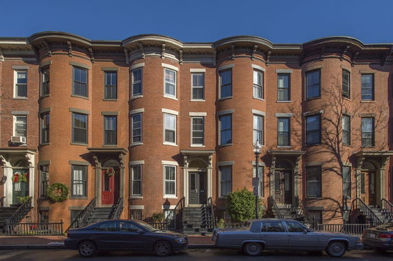 Front view of a row of brick townhouses with bay windows and small staircases leading to each entrance.