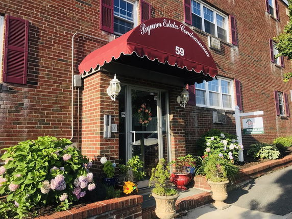 Front view of a condominium entrance with a red awning and brick exterior.
