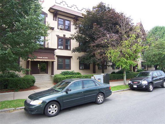 Front view of a multi-story residential building with cars parked on the street.