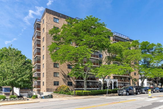 Front view of a multi-story apartment building with balconies and trees lining the street.