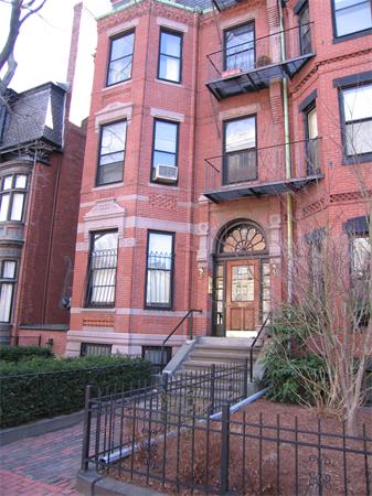 Front view of a red-brick multi-story building with balconies and decorative window frames.