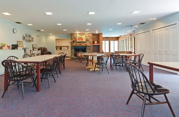 Interior of a club house with tables and chairs, a fireplace, and a small kitchenette.