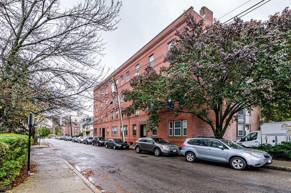 Front view of a four-story brick apartment building on a street corner.
