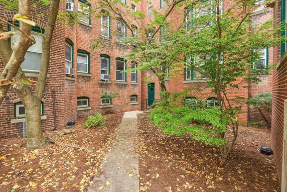 Exterior view of a brick multi-story building with windows and a path leading to a door.