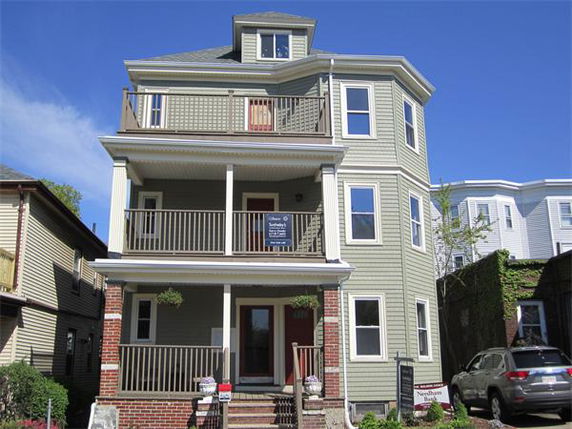 Front view of a three-story house with multiple balconies and a brick base.