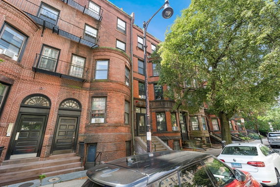 Front view of a multi-story brick building with arched doorways and fire escapes.