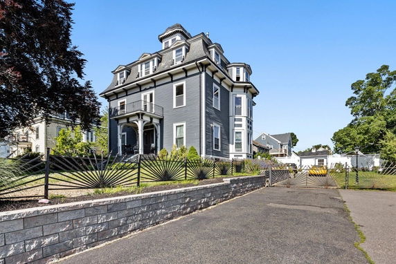 Front view of a large multi-story house with a mansard roof and a balcony.