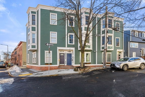 Front view of a three-story green townhouse on a street corner.