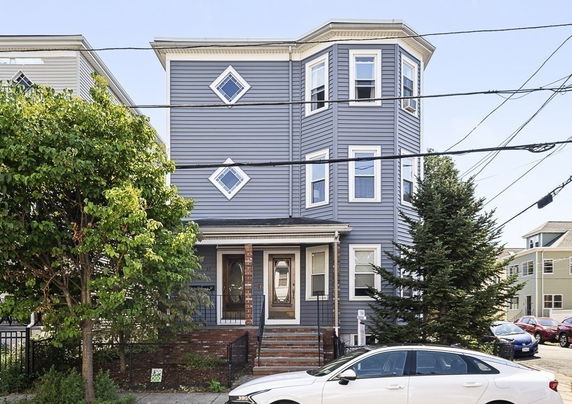 Front view of a multi-story blue house with bay windows.