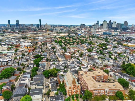 Wide aerial view of a cityscape with numerous residential and commercial buildings, and a central church building.