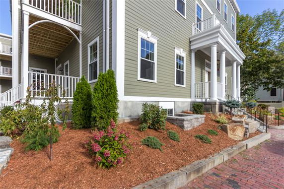 Front view of a two-story house with green siding and white trim, featuring a porch with columns.