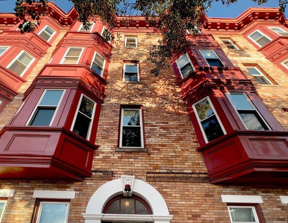 Front view of a multi-story brick building with red bay windows.