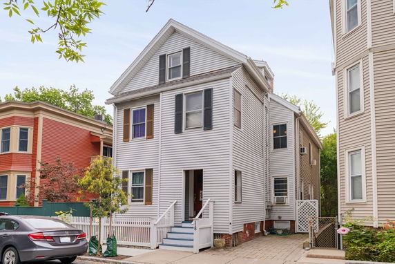 Front view of a multi-story house with white siding and black shutters.