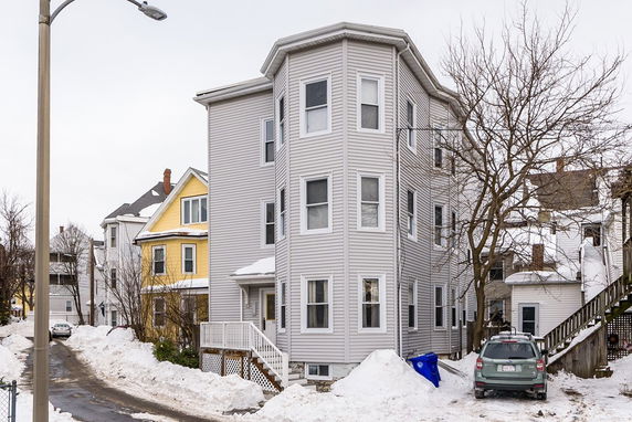Front view of a three-story house with a gray exterior and multiple windows on a snowy street.
