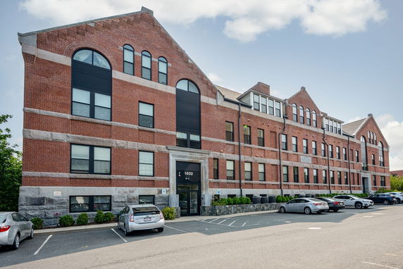Front view of a multi-story brick building with arched windows and a parking lot.