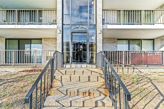 Front view of a multi-story condominium building with balconies and a central entrance.