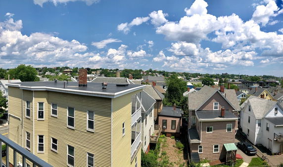Panoramic view of residential neighborhood with multiple houses and rooftops under a partly cloudy sky.