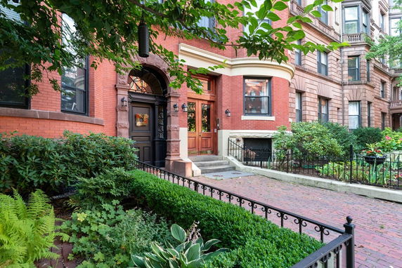 Front view of a red brick building with arched doorway and bay window.