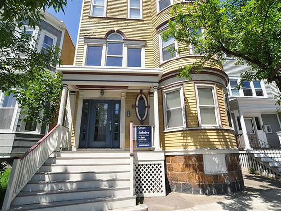 Front view of a multi-story house with yellow siding and arched windows.