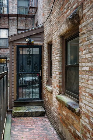Narrow passageway with a metal gate entrance to a brick building.