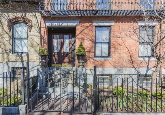 Front view of a brick house with iron fence and steps leading to the entrance.