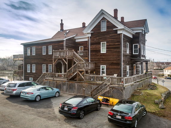 Front view of a large two-story wooden building with multiple entrances and parking area.
