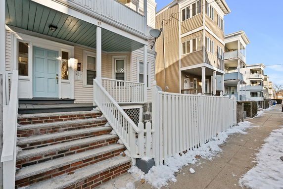 Front view of a multi-story residential building with a covered entryway and white fence.