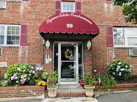 Front view of a brick condominium building entrance with an awning.