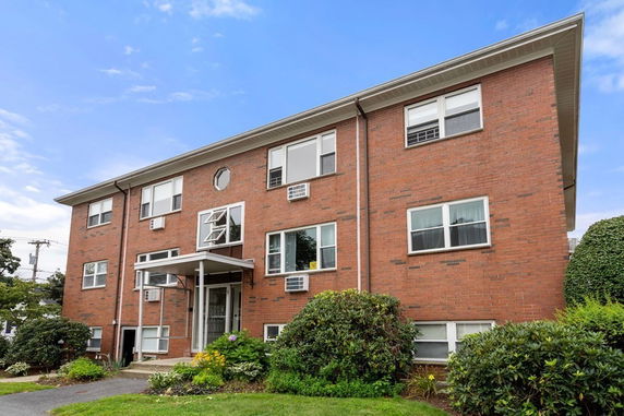 Front view of a three-story brick apartment building with multiple windows and a small entrance canopy.