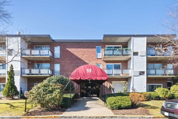 Front view of a three-story apartment building with balconies and a red awning entrance.