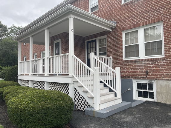 Front view of a two-story brick house with a covered porch and white railings.