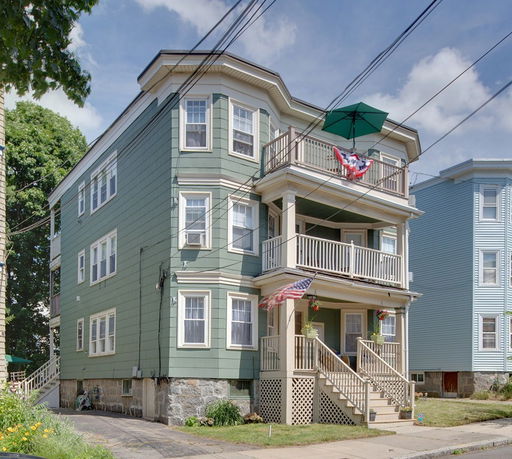 Front view of a multi-story green house with multiple balconies and a staircase leading to the entrance.