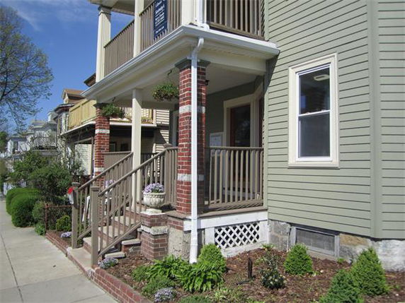 Front view of a multi-story house with a front porch and brick pillars.