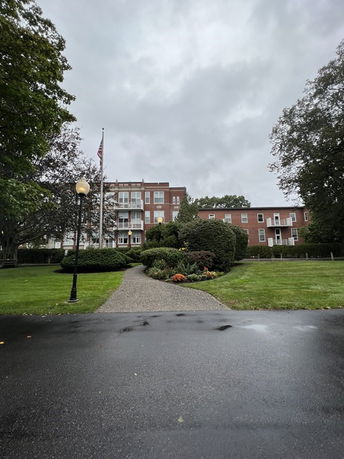 Front view of a multi-story brick building with a paved walkway leading to it.