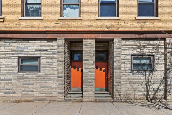 Front view of a building with stone and brick facade featuring two red doors.