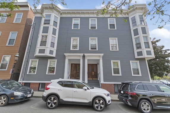 Front view of a multi-story grey building with bay windows and a small entrance porch.