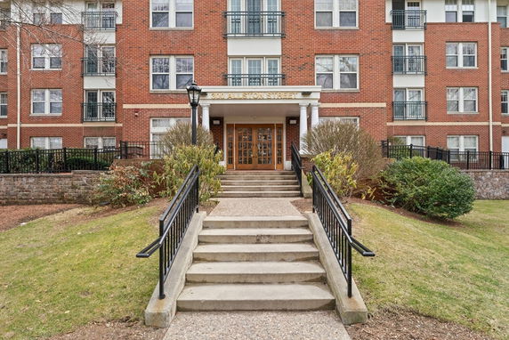 Front view of a multi-story brick building with a central entrance featuring columns and steps leading up.