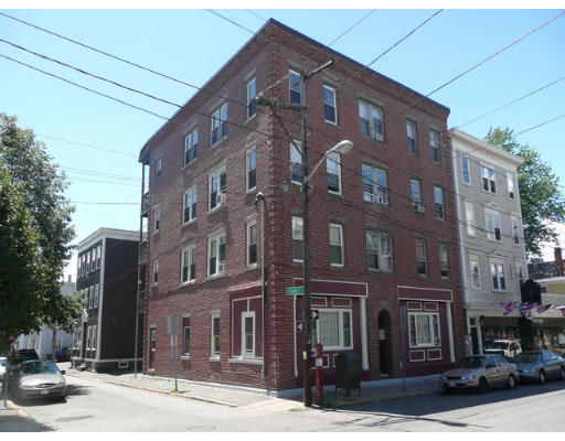 Front and side view of a four-story brick building on a street corner.