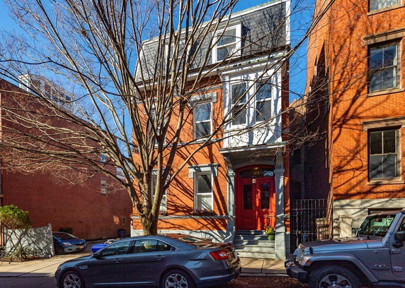 Front view of a three-story brick house with a prominent tree in front.