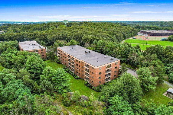 Aerial view of a four-story apartment building surrounded by dense trees and greenery.