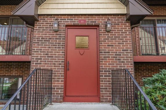 Front view of a brick building with a red door and railings.