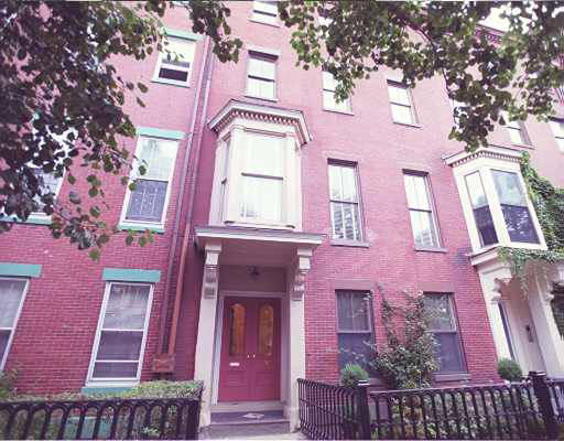Front view of a multi-story brick apartment building with bay windows and a red door.