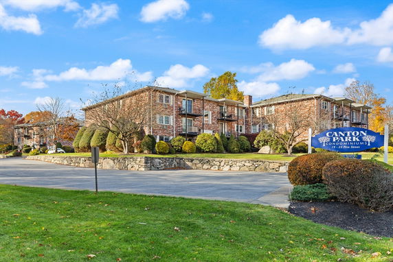 Front view of a brick condominium complex with adjacent parking area.