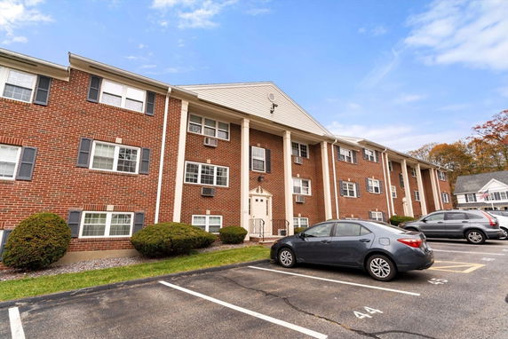 Front view of a multi-story brick building with columns and parking spaces in front.