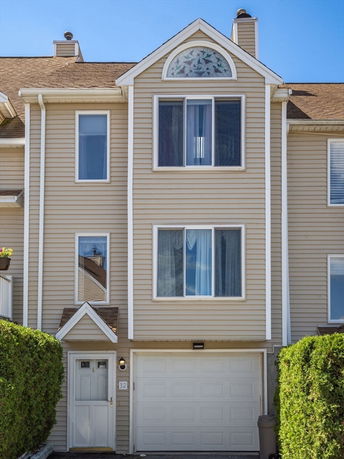 Front view of a three-story townhouse with beige siding and a single garage.