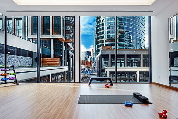 Interior view of a fitness area with large windows overlooking city buildings.