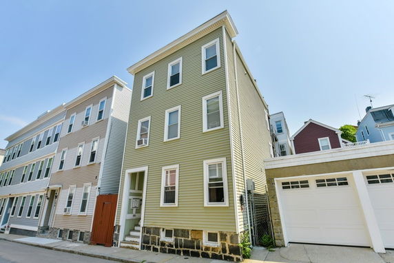 Front view of a multi-story residential building with light-colored siding and a garage.