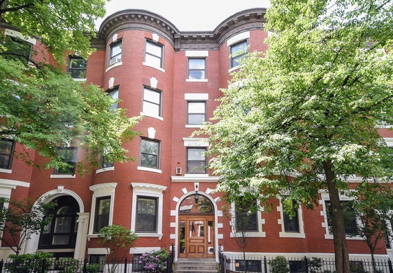 Front view of a brick apartment building with arched windows and wooden door.