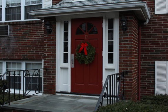 Front entrance of a brick house with a red door and wreath.